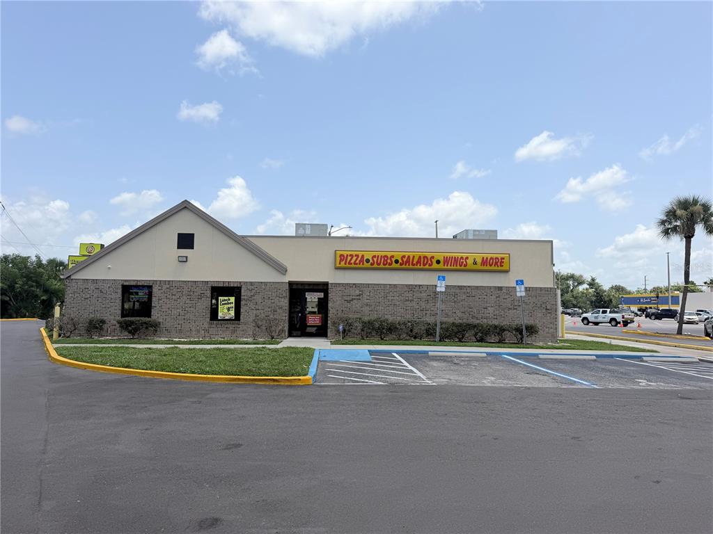 A single-story brick commercial building with a yellow sign advertising pizza, subs, and wings — 2439 ENTERPRISE ROAD, ORANGE CITY, FL
