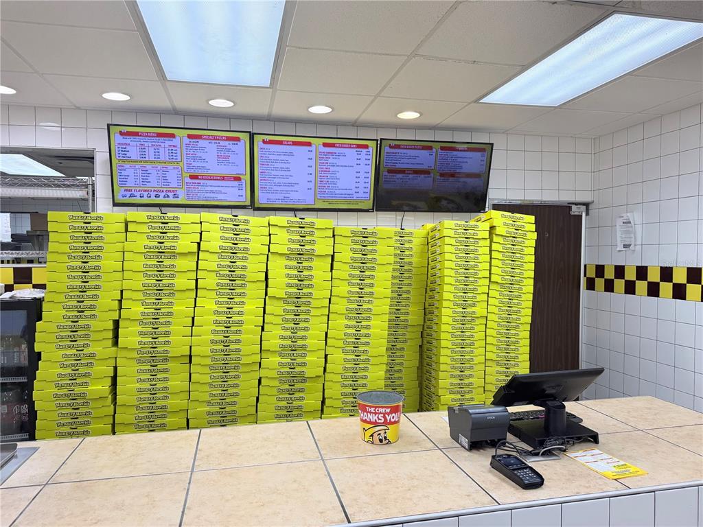 A Hungry Howie's pizza restaurant counter features stacks of yellow pizza boxes and digital menu boards — 2439 ENTERPRISE ROAD, ORANGE CITY, FL