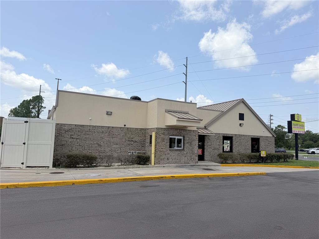 A single-story commercial building with a brick facade, drive-thru window, and a white privacy fence — 2439 ENTERPRISE ROAD, ORANGE CITY, FL
