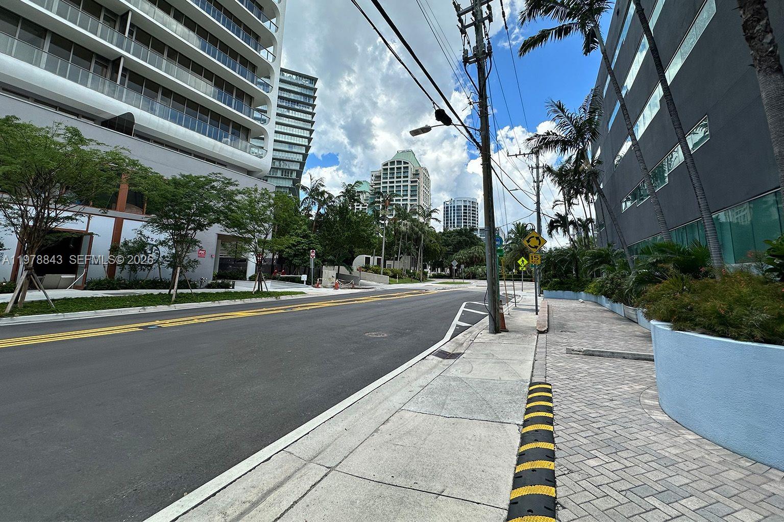 A paved street runs between a modern high-rise building and a commercial structure with palm trees — 2699 Tigertail Ave # 14, Miami FL 33133, MIAMI, FL