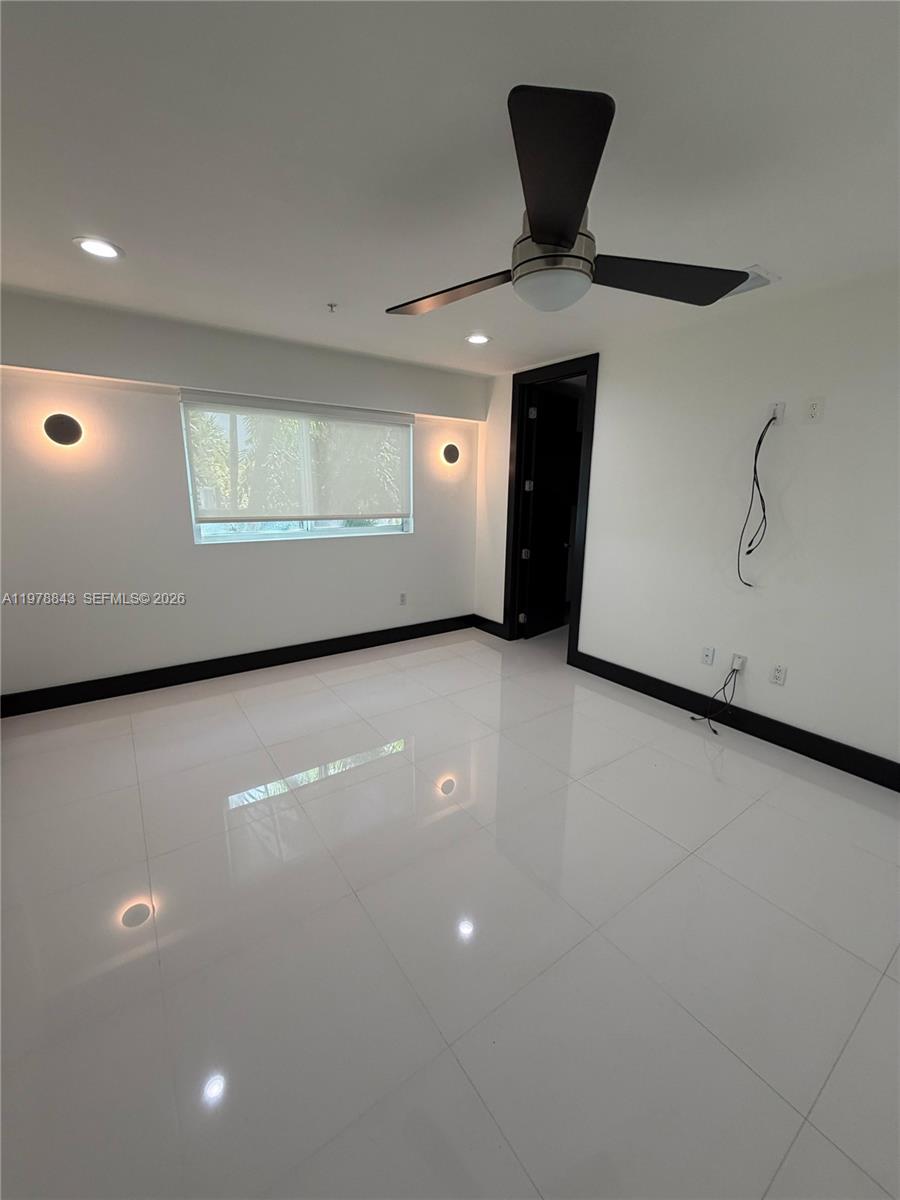 A minimalist bedroom features white tile flooring, a ceiling fan, and black trim accents — 2699 Tigertail Ave # 14, Miami FL 33133, MIAMI, FL