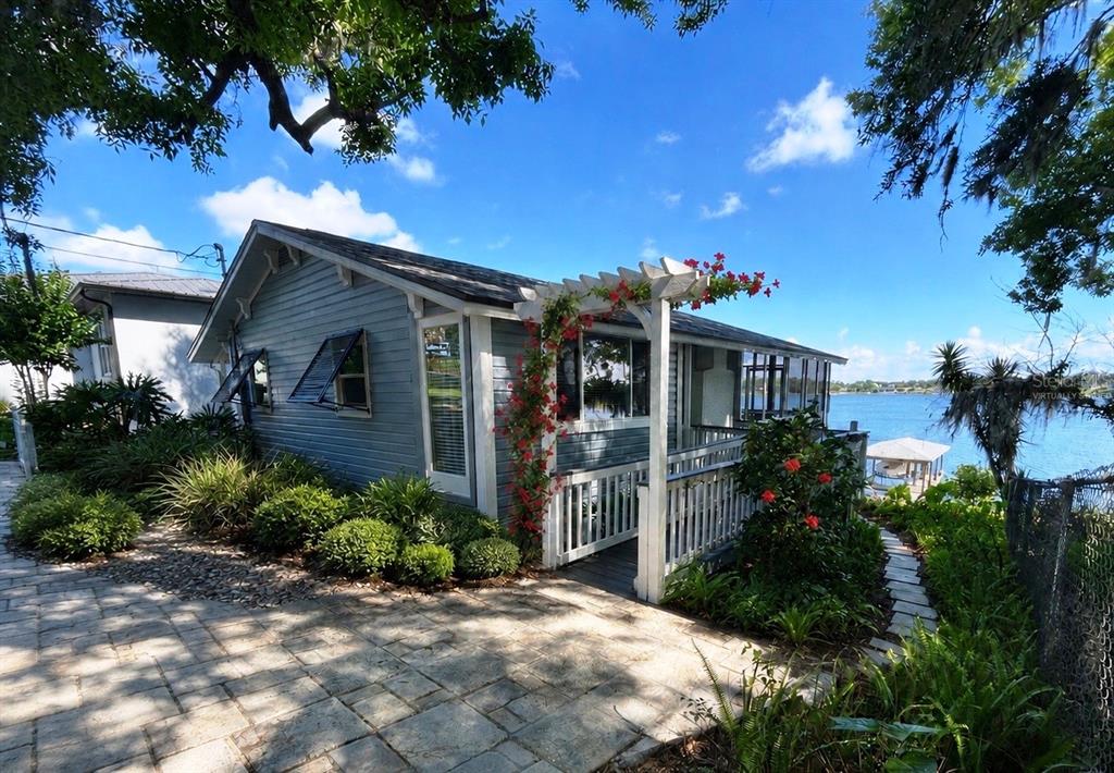 A blue cottage with a white pergola and porch overlooks a lake on a sunny day — 16533 LOWRY ROAD, MONTVERDE, FL