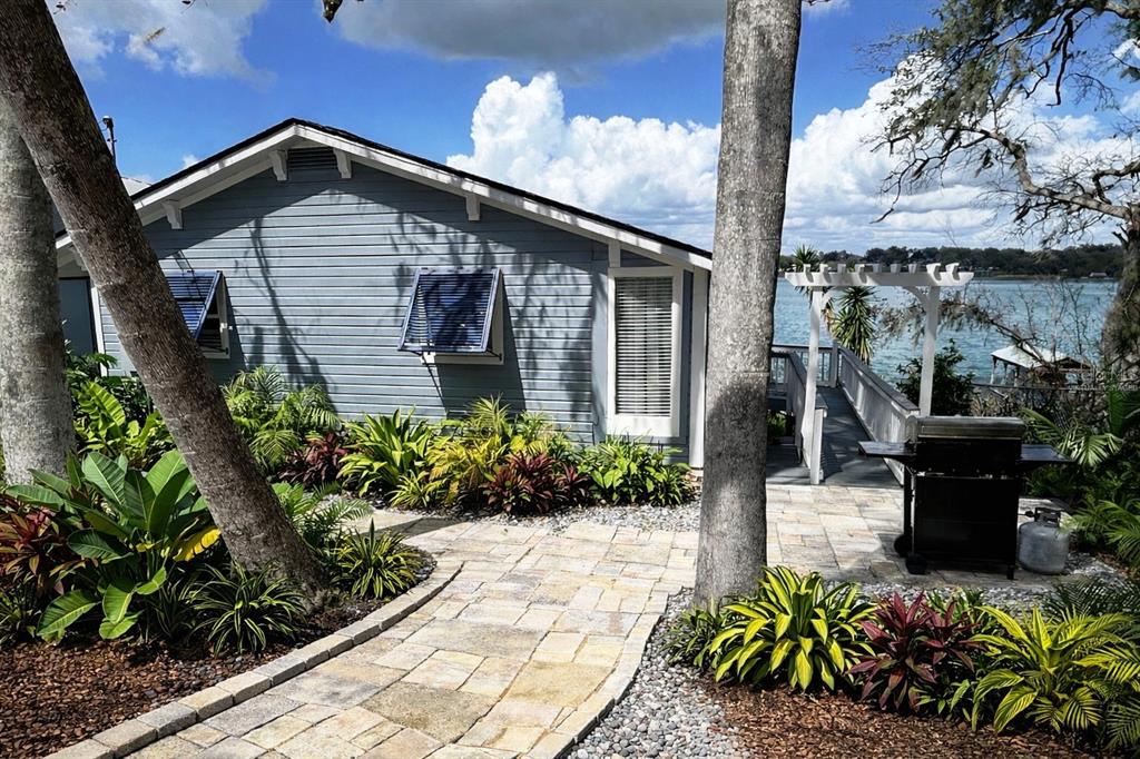A blue house with a stone walkway, tropical landscaping, and a grill overlooking a lake — 16533 LOWRY ROAD, MONTVERDE, FL