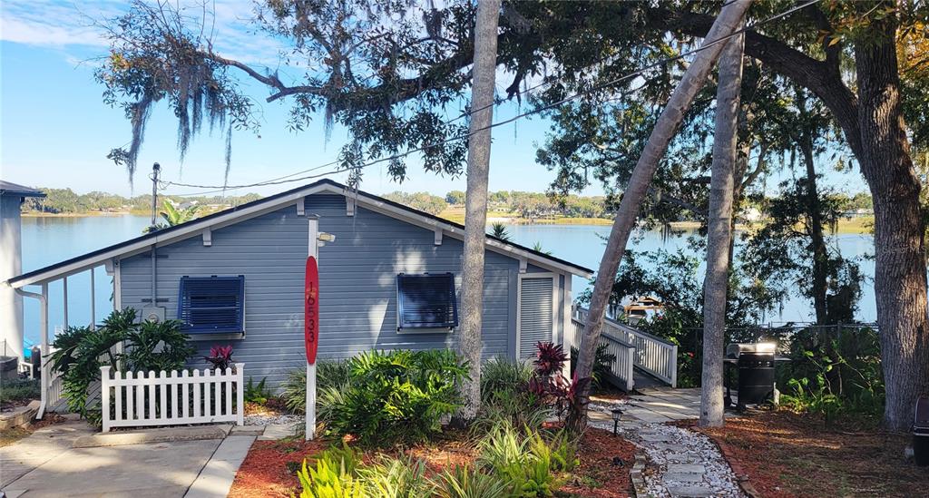 A blue house with a white picket fence sits on a lot overlooking a lake — 16533 LOWRY ROAD, MONTVERDE, FL