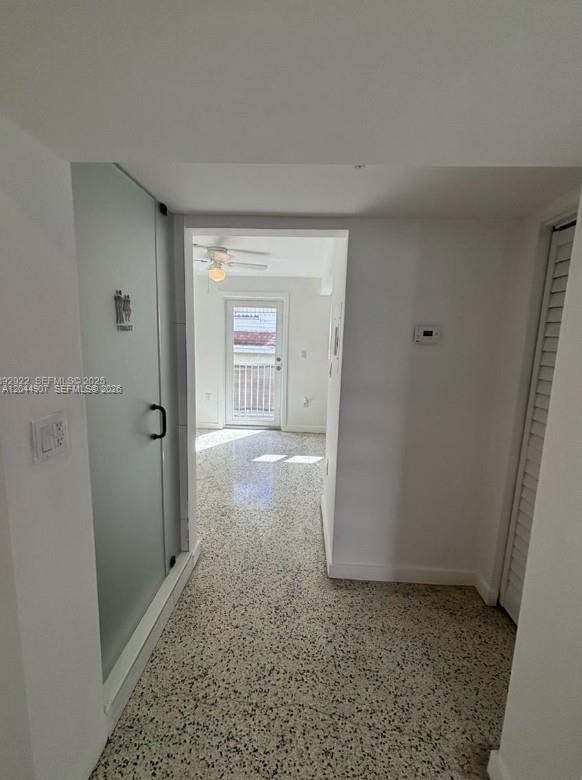 A hallway with terrazzo flooring leads to a room with a glass-doored bathroom — 560 NW 1st St # 7, Miami FL 33128, MIAMI, FL