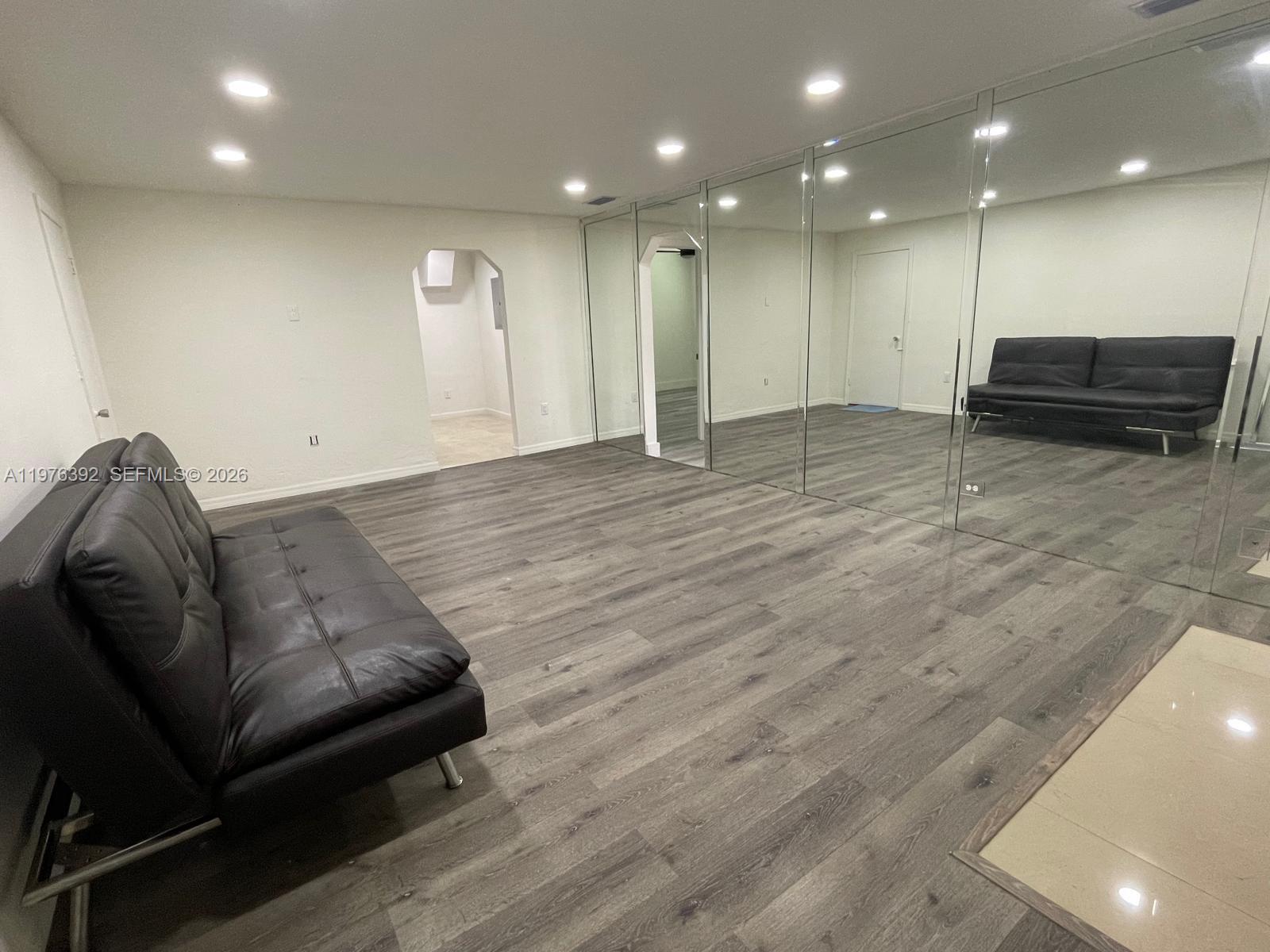A room with wood-look flooring, a black sofa, and a wall of floor-to-ceiling mirrors — 10415 NW 35th Ave, Miami FL 33147, MIAMI, FL