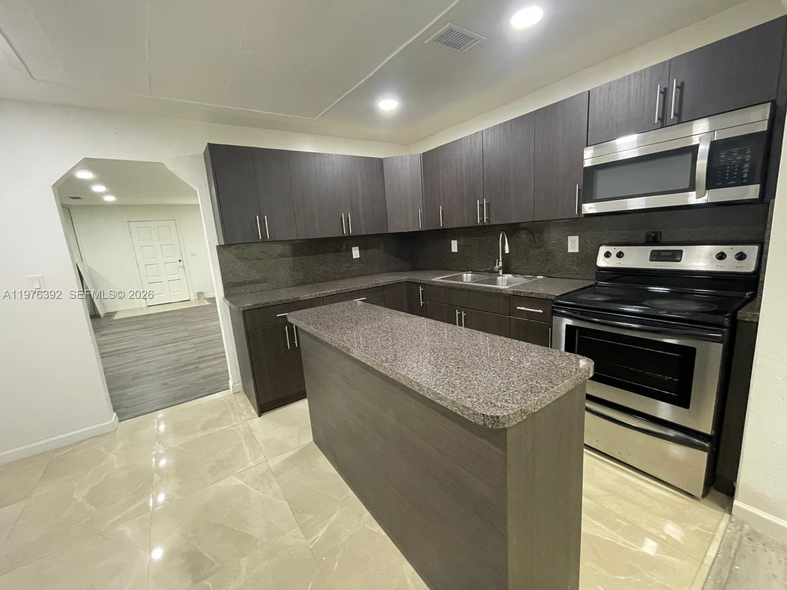 A kitchen features dark wood cabinets, granite countertops, stainless steel appliances, and light tile flooring — 10415 NW 35th Ave, Miami FL 33147, MIAMI, FL