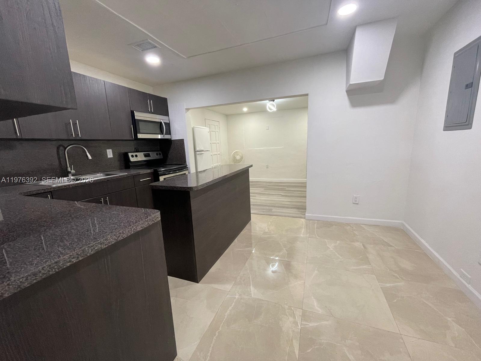 A kitchen features dark wood cabinets, granite countertops, and light-colored tile flooring — 10415 NW 35th Ave, Miami FL 33147, MIAMI, FL