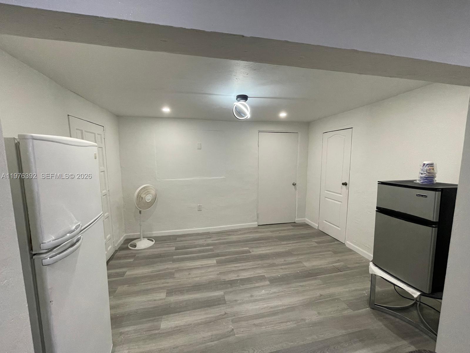 A room with white walls, gray wood-look flooring, two refrigerators, and two closed doors — 10415 NW 35th Ave, Miami FL 33147, MIAMI, FL