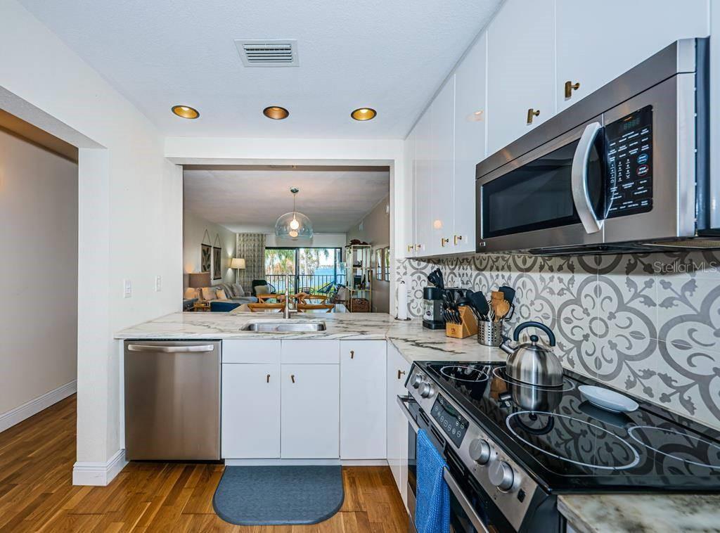 A kitchen with white cabinets, stainless steel appliances, marble countertops, and a patterned tile backsplash — 6295 BAHIA DEL MAR CIRCLE UNIT 216, ST PETERSBURG, FL