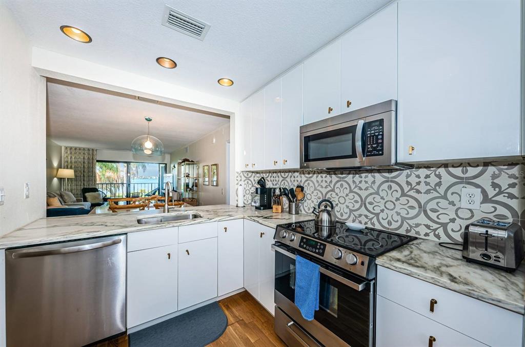 A kitchen with white cabinets, marble-look countertops, patterned backsplash, and stainless steel appliances — 6295 BAHIA DEL MAR CIRCLE UNIT 216, ST PETERSBURG, FL