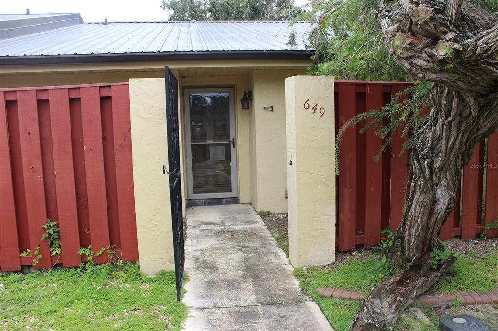 A concrete walkway leads to a front door framed by a red fence and stucco pillars — 649 BROADMOOR CIRCLE, WINTER HAVEN, FL