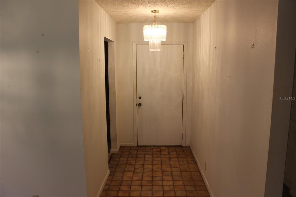 A tiled entryway features a white front door and a crystal chandelier hanging from above — 649 BROADMOOR CIRCLE, WINTER HAVEN, FL