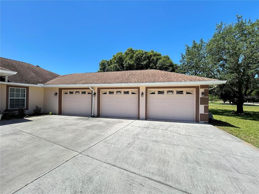 A three-car garage with light-colored doors and a concrete driveway under a clear blue sky — 1921 FLOWER TERRACE, SEBRING, FL