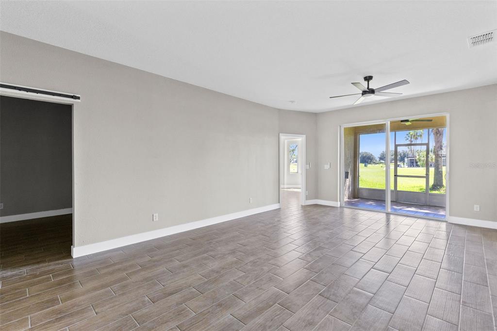 An empty living room features wood-look tile flooring, a ceiling fan, and sliding glass doors — 183 CLUB VILLAS LANE, KISSIMMEE, FL