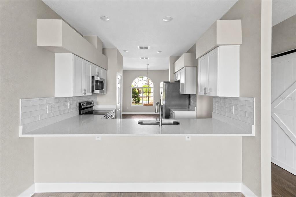 A kitchen with white cabinets, stainless steel appliances, and a breakfast bar overlooking a window — 183 CLUB VILLAS LANE, KISSIMMEE, FL