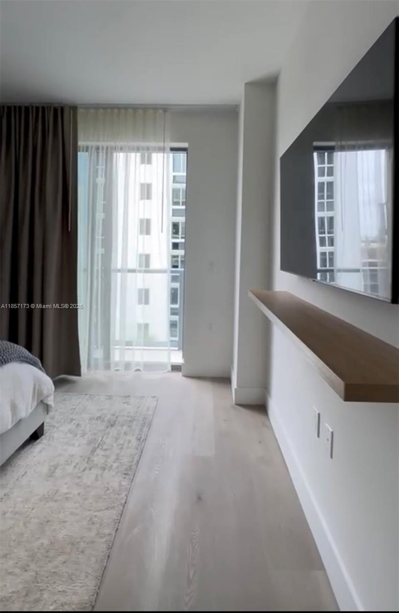 A bedroom features a wall-mounted television, a floating wooden shelf, and a balcony with curtains — 229 SW 9th St # 403, Miami FL 33130, MIAMI, FL