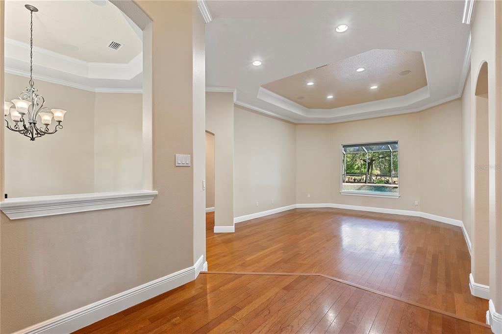 A living room with hardwood floors, a tray ceiling, and a view of a pool — 8297 DAY LILY PLACE, SANFORD, FL