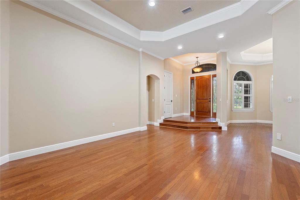 An empty room with hardwood floors, a tray ceiling, and a raised entryway with doors — 8297 DAY LILY PLACE, SANFORD, FL
