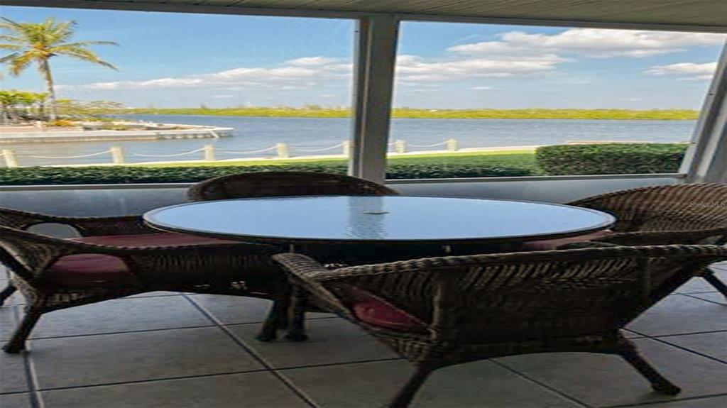 A screened-in patio features a glass-topped dining table and wicker chairs overlooking a waterfront view — 1365 SIESTA BAYSIDE DRIVE UNIT 1365-C, SARASOTA, FL