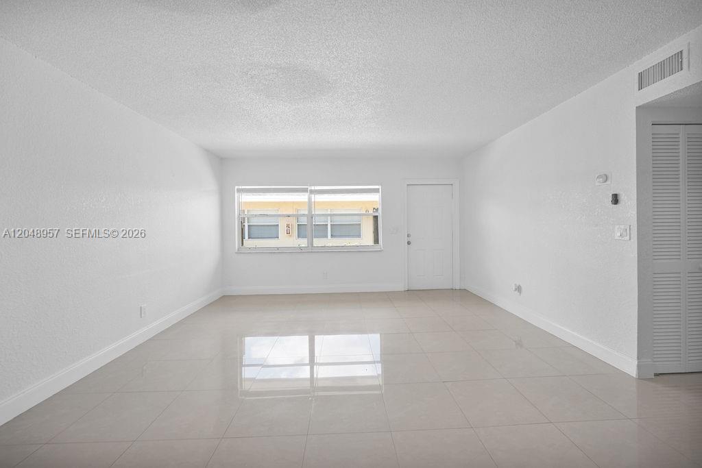 An empty room with white walls, light-colored tile flooring, and a window overlooking a building — 664 SW Kathy Ct, Margate FL 33068, MARGATE, FL