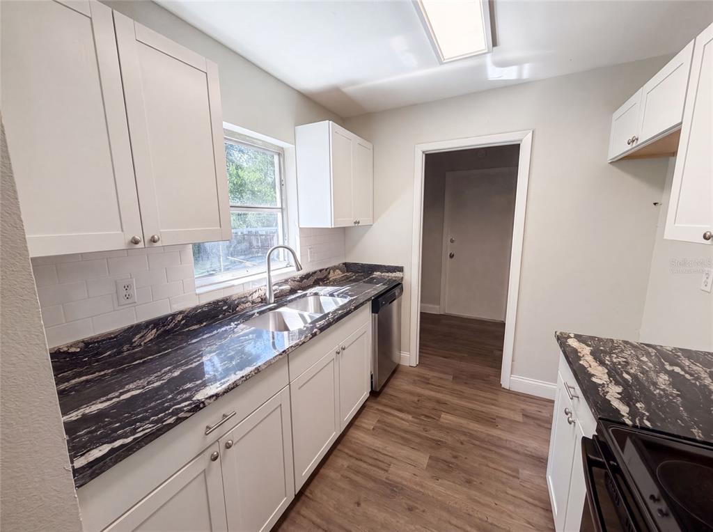 A kitchen features white shaker cabinets, black granite countertops, and wood-look flooring — 5064 BROMLEY AVENUE, SPRING HILL, FL