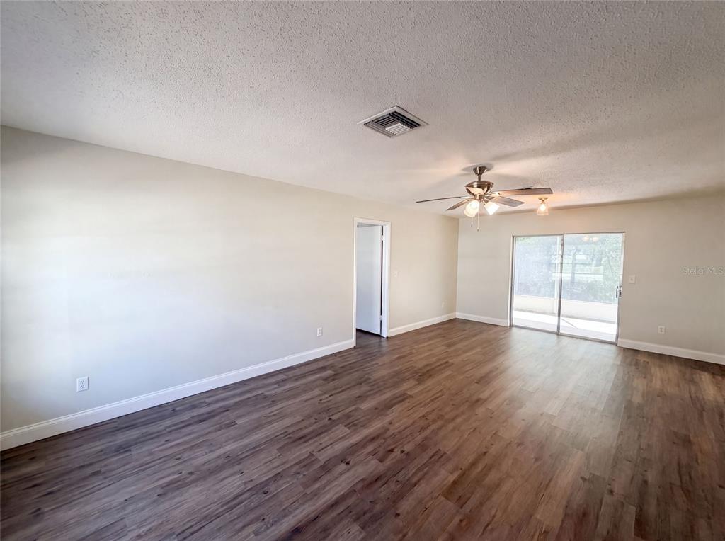 An empty living room features light-colored walls, wood-look flooring, a ceiling fan, and sliding glass doors — 5064 BROMLEY AVENUE, SPRING HILL, FL