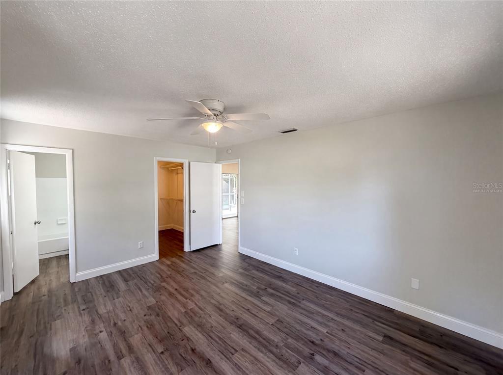 A bedroom with light gray walls, wood-look flooring, a ceiling fan, and two open doorways — 5064 BROMLEY AVENUE, SPRING HILL, FL