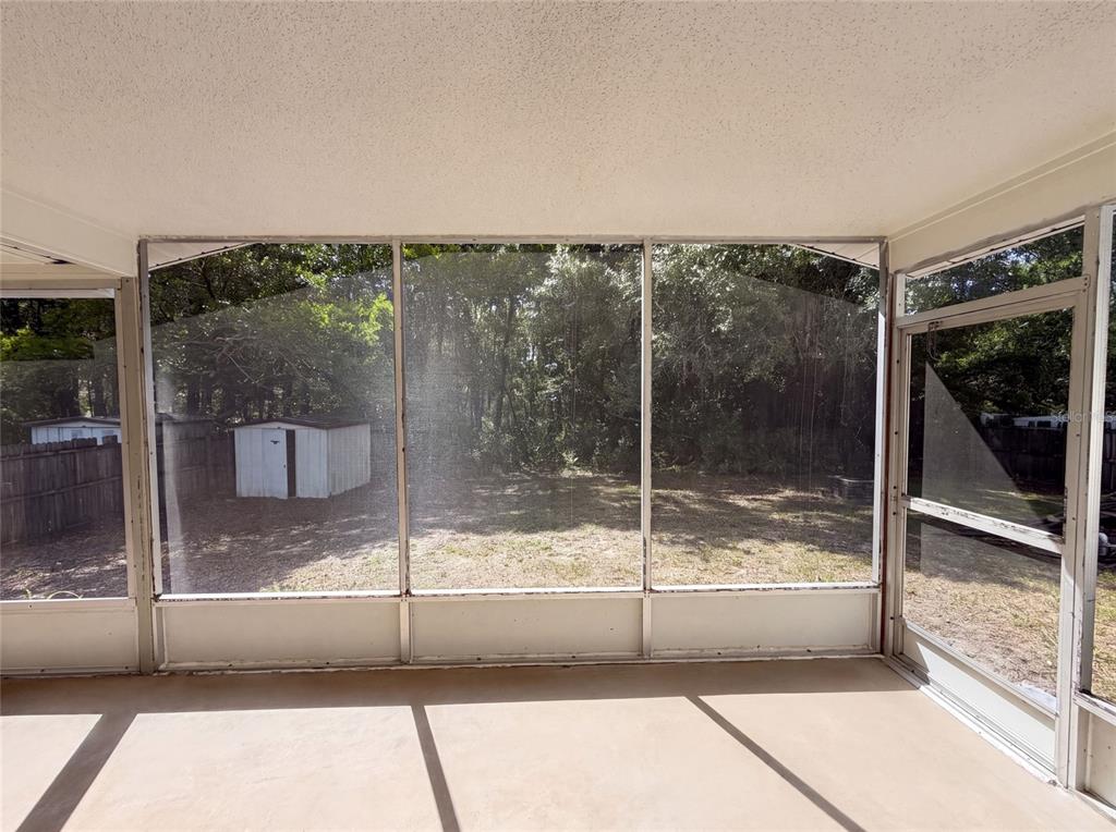 A screened-in porch overlooks a backyard with a small shed and wooded area — 5064 BROMLEY AVENUE, SPRING HILL, FL