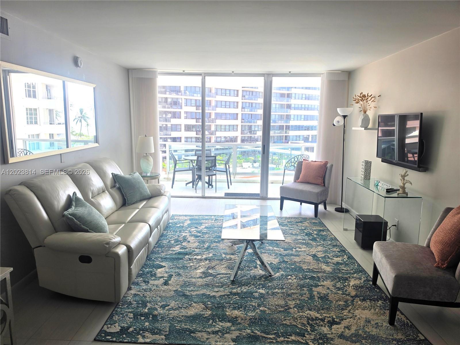 A living room features a white leather sofa, blue patterned rug, and a glass balcony door — 5161 Collins Ave # 502, Miami Beach FL 33140, MIAMI BEACH, FL