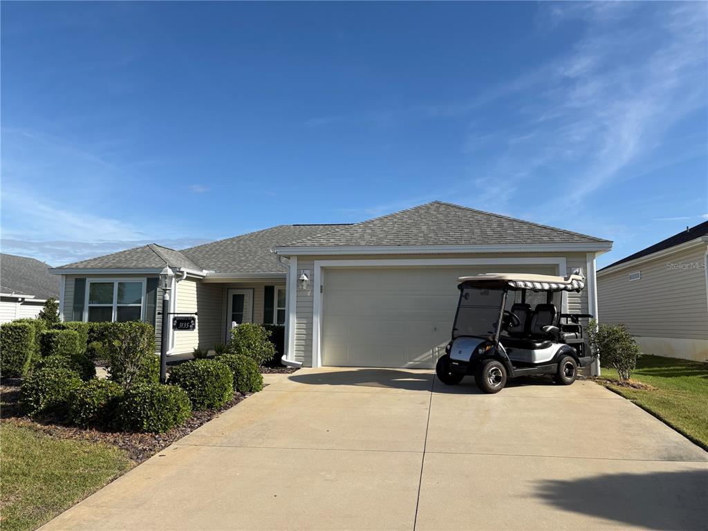 A single-story house with a beige exterior, a two-car garage, and a golf cart parked outside — 3135 BURNS DRIVE, THE VILLAGES, FL