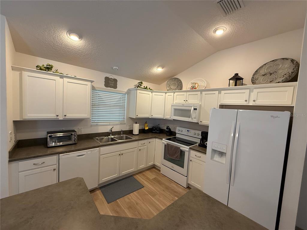 A kitchen features white cabinets, dark countertops, stainless steel appliances, and light wood-look flooring — 3135 BURNS DRIVE, THE VILLAGES, FL