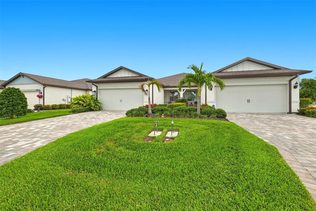 A single-story house with two garage doors and a paved driveway sits behind a lawn — 10208 COASTAL SHORES DRIVE, PARRISH, FL