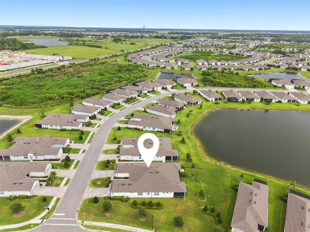 An aerial view shows a residential neighborhood with houses, a pond, and green space — 10208 COASTAL SHORES DRIVE, PARRISH, FL