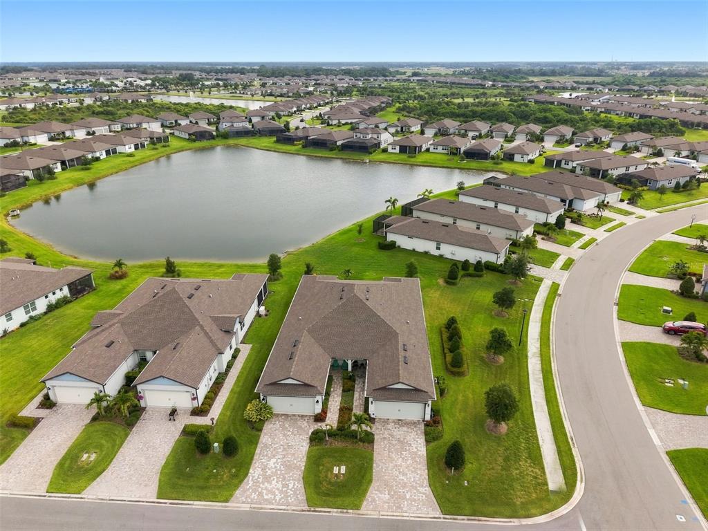 An aerial view shows suburban houses with brown roofs situated near a large retention pond — 10208 COASTAL SHORES DRIVE, PARRISH, FL