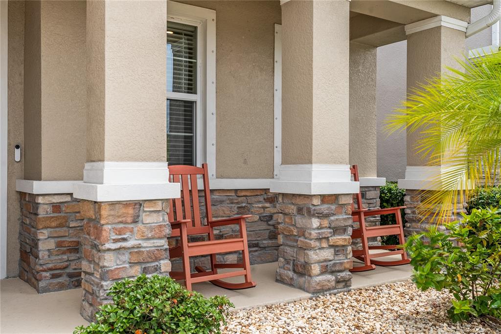 Two red rocking chairs sit on a covered porch with stone-based pillars — 17727 CANTARINA COVE, BRADENTON, FL
