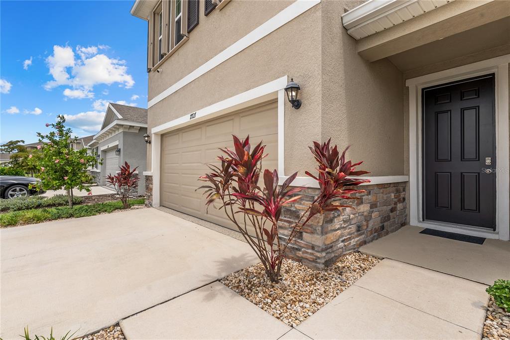 A beige house exterior features a tan garage door, stone accents, and a black front door — 17727 CANTARINA COVE, BRADENTON, FL