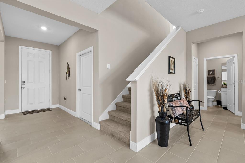 A tiled entryway features a staircase, a white front door, and a small decorative bench — 17727 CANTARINA COVE, BRADENTON, FL