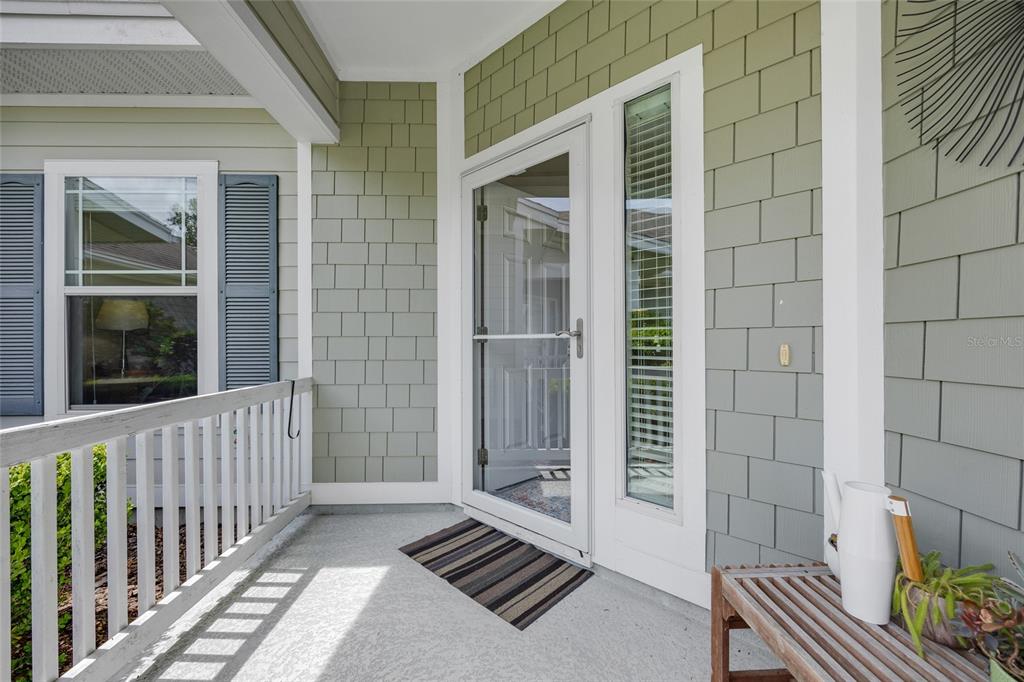 A covered porch features light green shingle siding, a white storm door, and a wooden bench — 12656 NW 11TH PLACE, NEWBERRY, FL