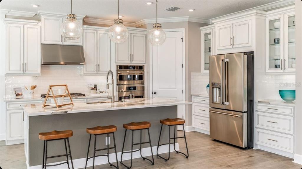 A modern kitchen features white cabinetry, stainless steel appliances, a gray island, and wooden bar stools — 827 JUNONIA BOULEVARD, NEW SMYRNA BEACH, FL