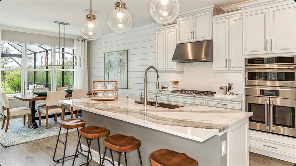 A modern kitchen features a large marble-topped island, white cabinetry, and a dining area nearby — 827 JUNONIA BOULEVARD, NEW SMYRNA BEACH, FL