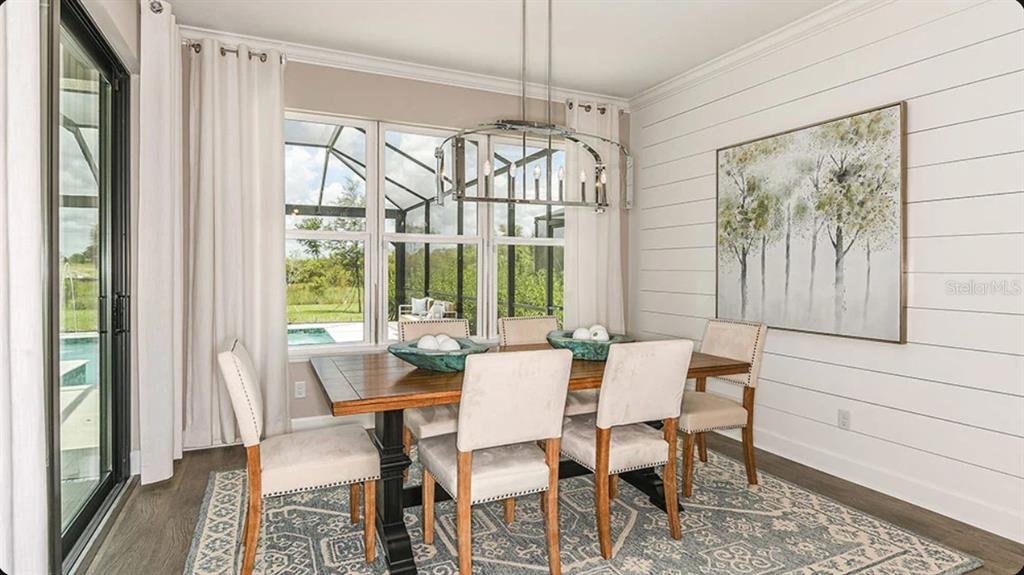 A dining room features a wooden table, upholstered chairs, a shiplap wall, and large windows — 827 JUNONIA BOULEVARD, NEW SMYRNA BEACH, FL