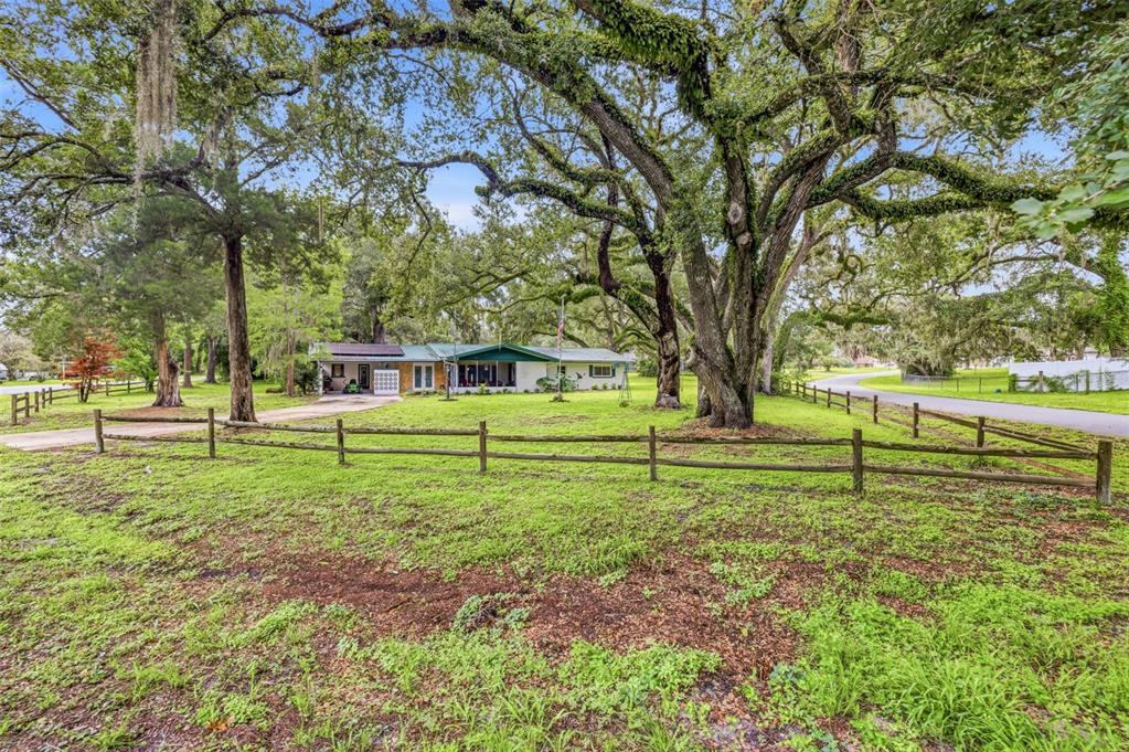 A single-story house sits behind a wooden split-rail fence under large, moss-covered oak trees — 34746 GARDENIA WAY, DADE CITY, FL