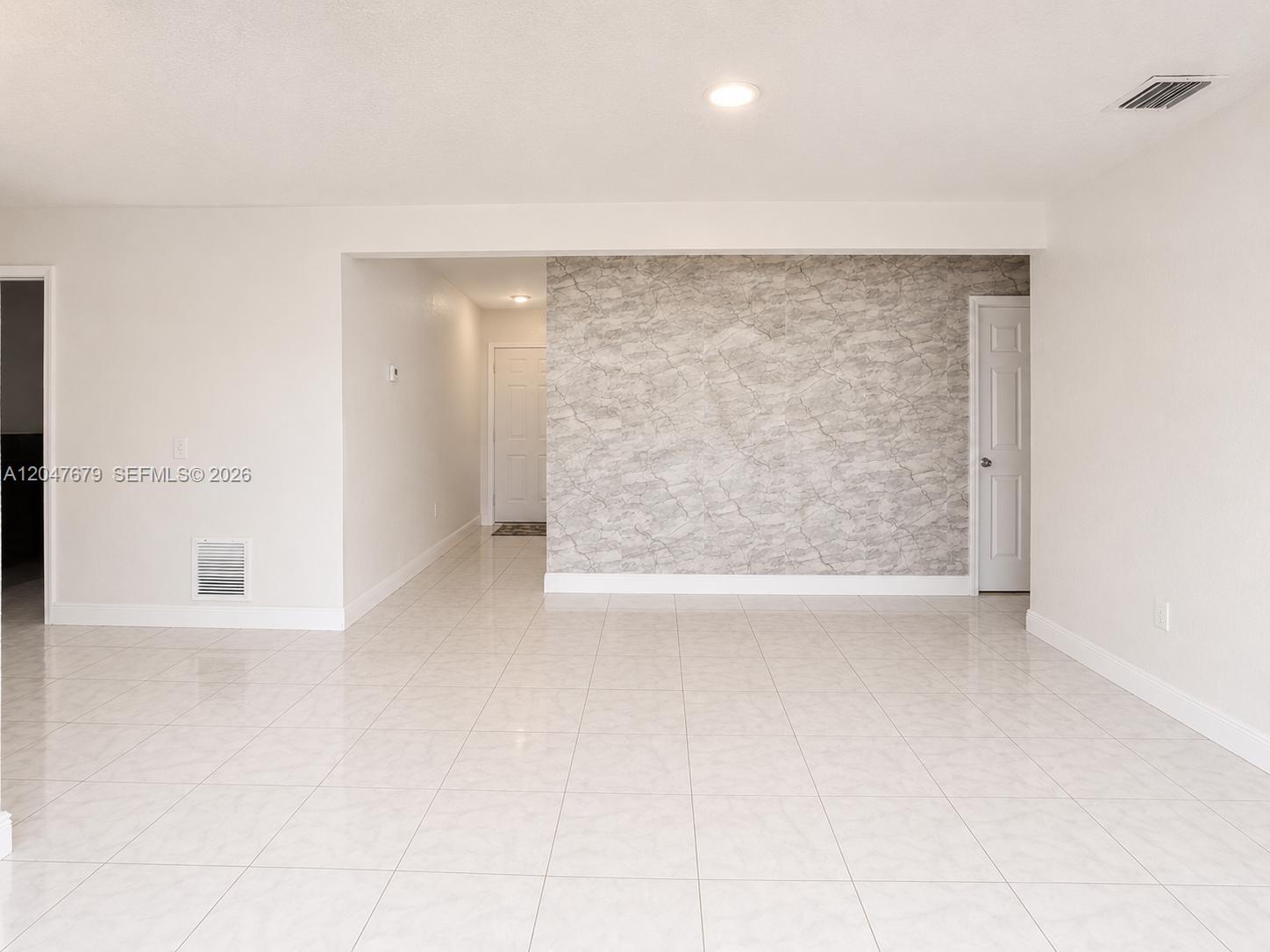 A bright, empty room features white tile flooring and a gray marble-patterned accent wall — 7612 Plantation Blvd, Miramar FL 33023, MIRAMAR, FL