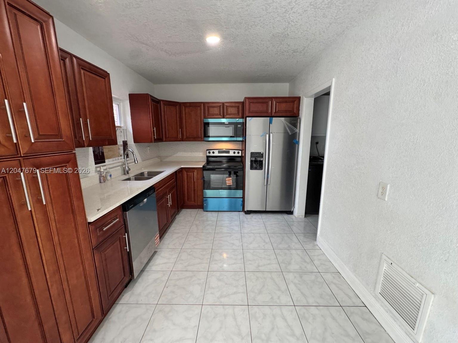 A kitchen features wood cabinets, stainless steel appliances, white countertops, and light-colored tiled flooring — 7612 Plantation Blvd, Miramar FL 33023, MIRAMAR, FL