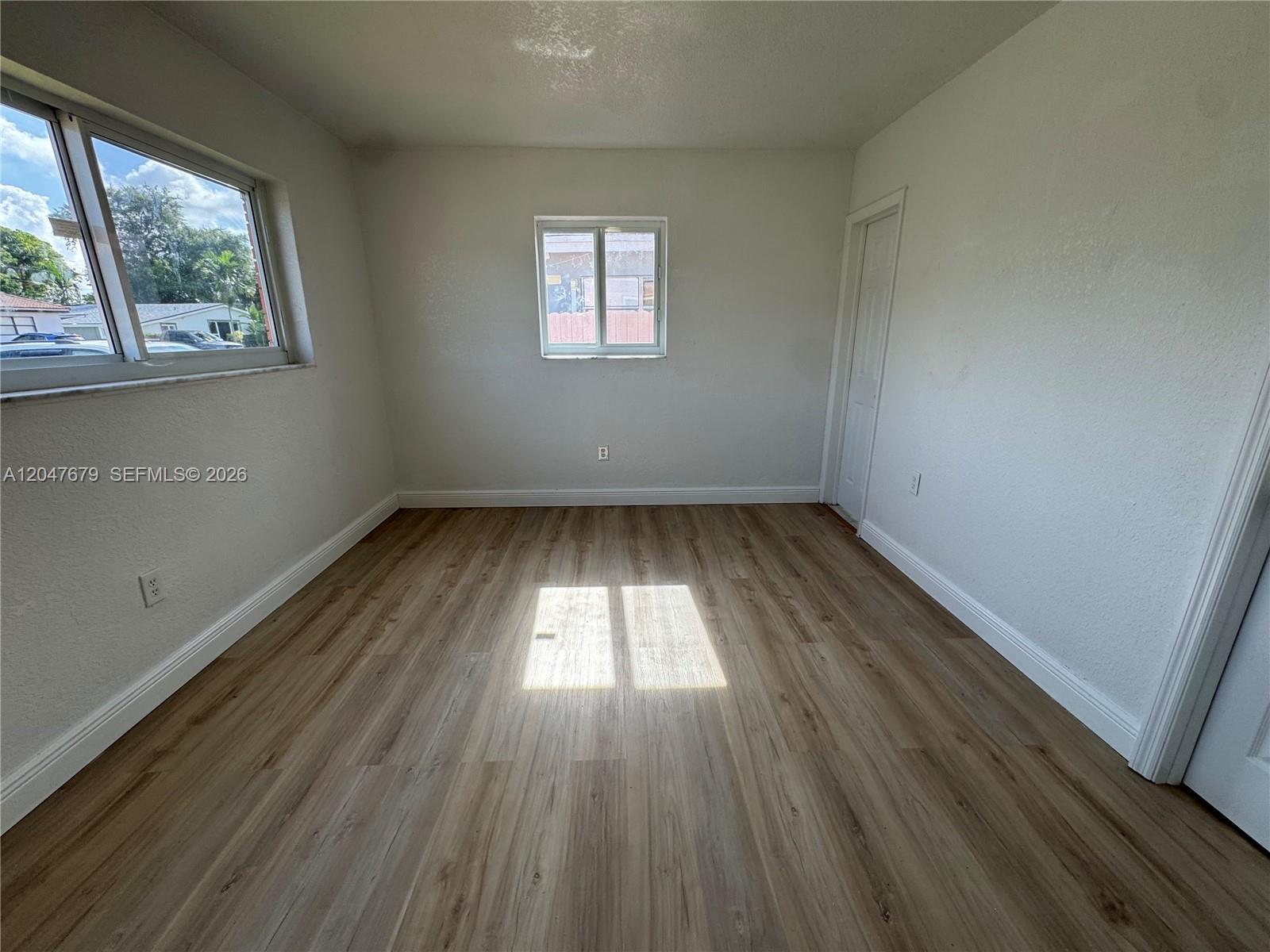 An empty room features light wood-look flooring, white walls, and two windows — 7612 Plantation Blvd, Miramar FL 33023, MIRAMAR, FL