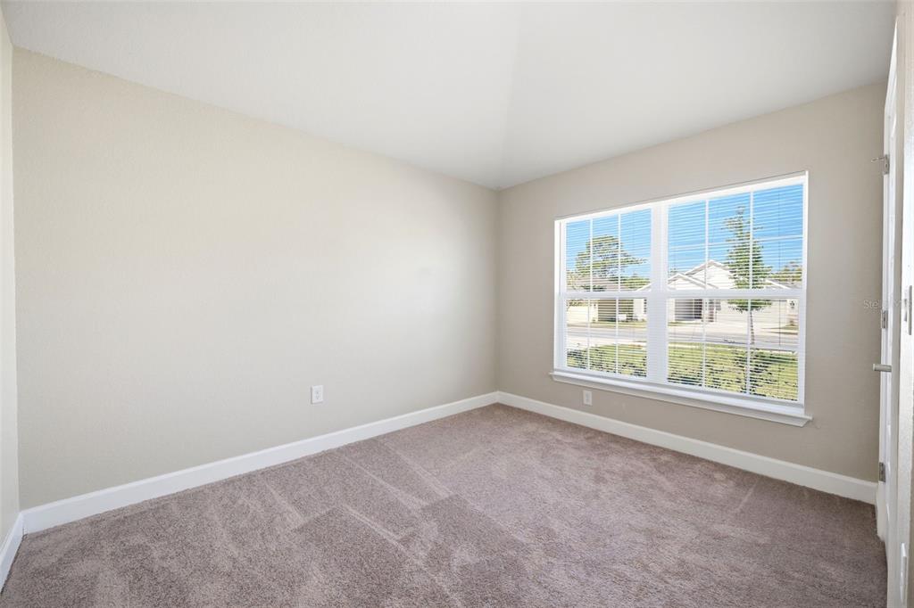 An empty bedroom features beige walls, tan carpeting, white trim, and a large window — 5524 OCEAN BREEZE DRIVE, SPRING HILL, FL