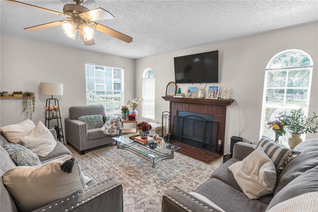 A living room features a brick fireplace, gray sofas, a glass coffee table, and windows — 11942 SKYLAKE PLACE UNIT C, TAMPA, FL