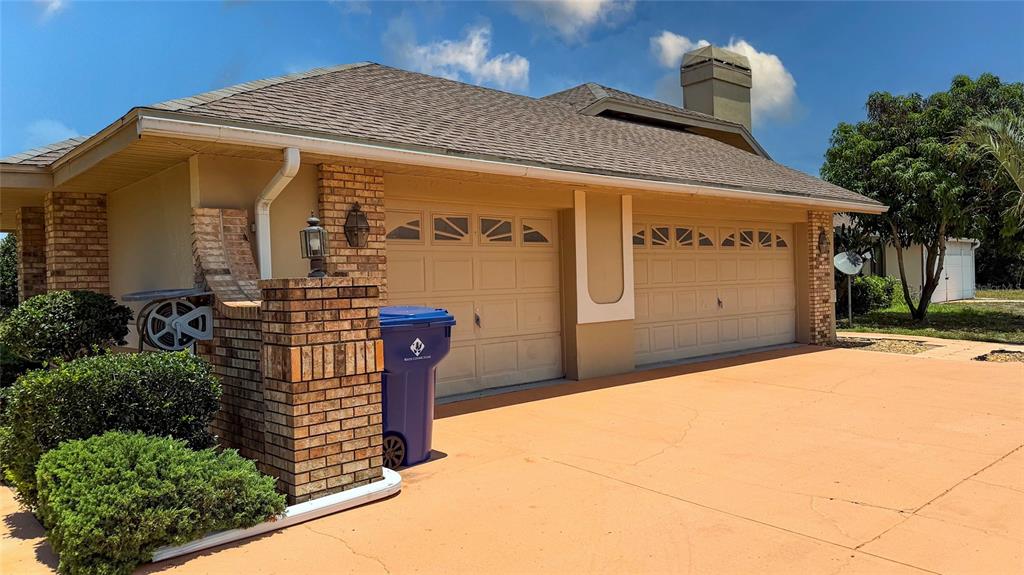A tan house with a two-car garage and a brick pillar sits on a driveway — 8732 SKYMASTER DRIVE, NEW PORT RICHEY, FL