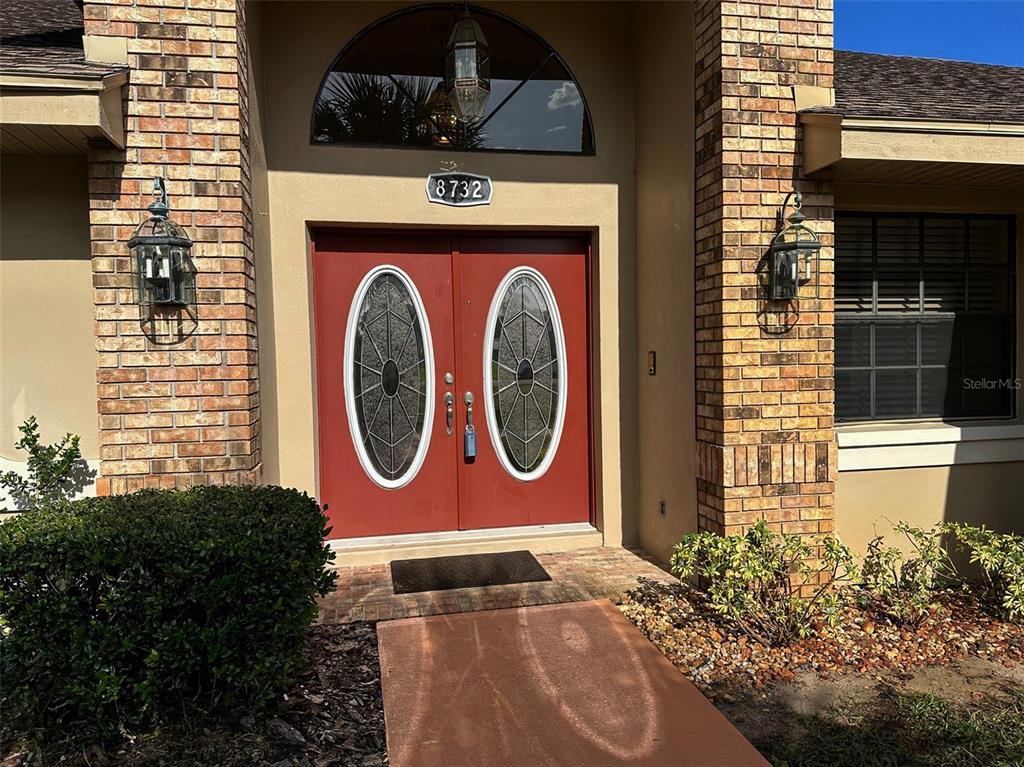A red double front door with oval glass inserts is framed by brick pillars — 8732 SKYMASTER DRIVE, NEW PORT RICHEY, FL